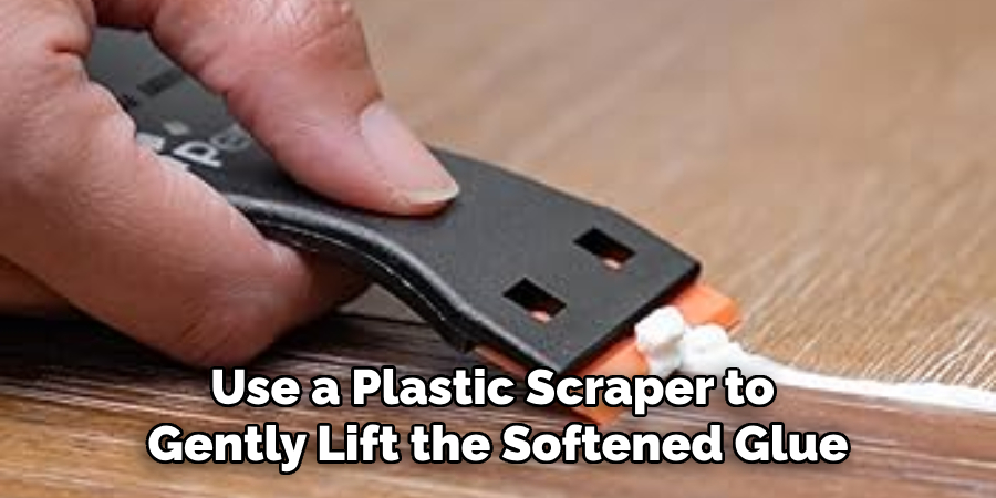 Use a Plastic Scraper or Razor Blade to Gently Lift the Softened Glue